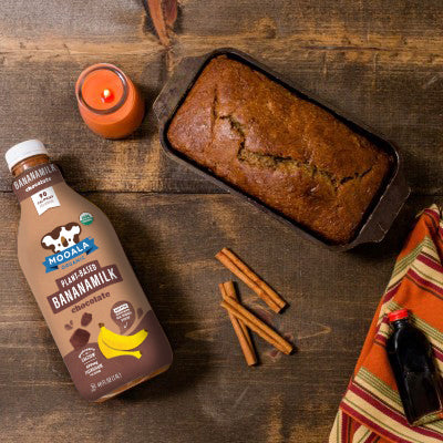 Chocolate Pumpkin Loaf, made with Mooala Chocolate Bananamilk, sitting on table with cinnamon sticks, a candle and a towel.